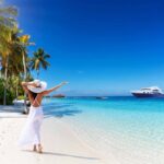 A Woman With White Hat Walks Down A Tropical Paradise Beach With Palm Trees And Turquoise Sea